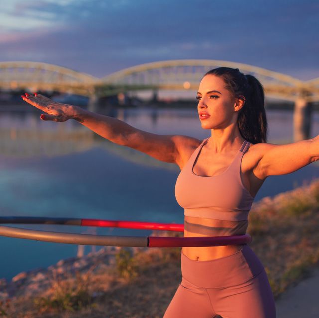 young woman doing hula hoop exercise at riverside in sunset