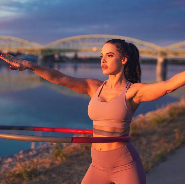 young woman doing hula hoop exercise at riverside in sunset