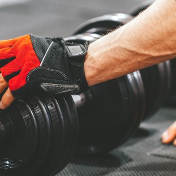 person with red weightlifting gloves reaching for dumbbell in gym