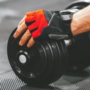 person with red weightlifting gloves reaching for dumbbell in gym