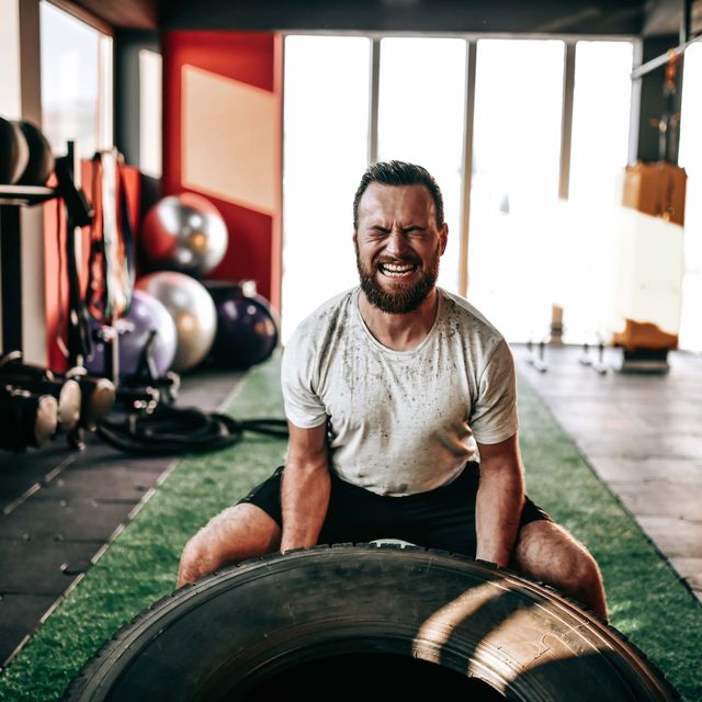 male athlete wincing with effort during truck tire gym workout