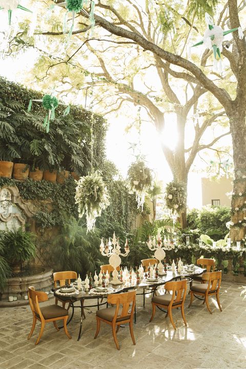 a series of sinuous bronze tone nesting tables is set for christmas dinner while spheres of greenery and florals shroud electrified chandeliers overhead