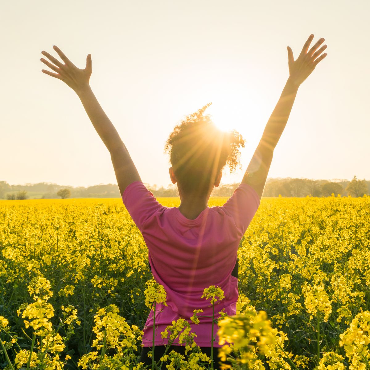 mixed race african american girl female young woman athlete runner teenager in golden sunset or sunrise arms raised celebrating in field of yellow flowers