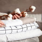 well groomed woman hands holding the cotton branch with pile of folded bed sheets and blankets