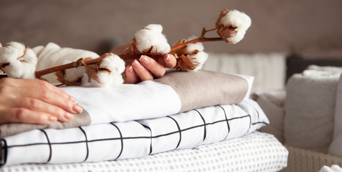well groomed woman hands holding the cotton branch with pile of folded bed sheets and blankets