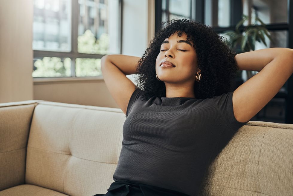 Well-being, peace and black woman relax on the sofa for health lifestyle, stress relief or healthy state of mind. Calm, dream and sleeping girl in the living room for rest, the comfortable break or the freedom of the mind