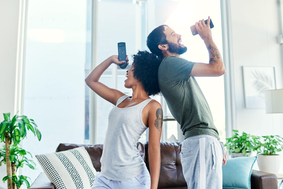 black woman and white man singing karaoke at home back to back