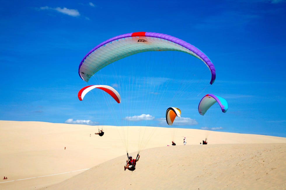 Een groepje paragliders zweeft over de zandkleurige kammen van La Grande Dune du Pyla