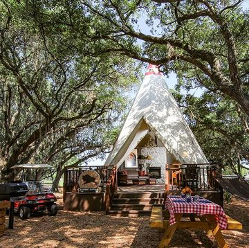 a teepee sits atop a front porch in a field of oak trees with a picnic table nearby