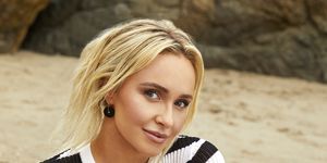 hayden panettiere sitting down on a beach towel, wearing a black and white striped top and black bikini bottoms