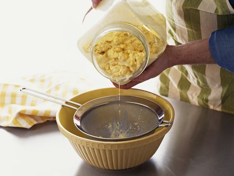 pouring churned butter into a strainer over a bowl to collect buttermilk, a byproduct of butter making
