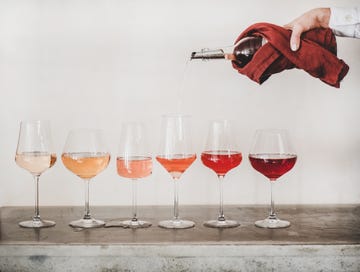 shades of rose wine in stemmed glasses placed in line from light to deep and womans hand pouring wine from bottle to glass