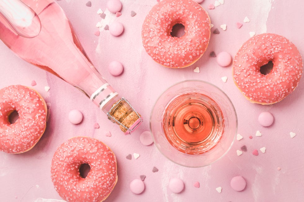 rose wine or cocktail with pink donuts and pink chocolate beans on pink background