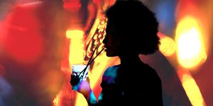 silhouette of a woman with afro hair drinking and in the background are blurred red and yellow lights