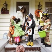 woman distributing candy to costumed children before sunset, the earliest time trick or treating usually starts on halloween