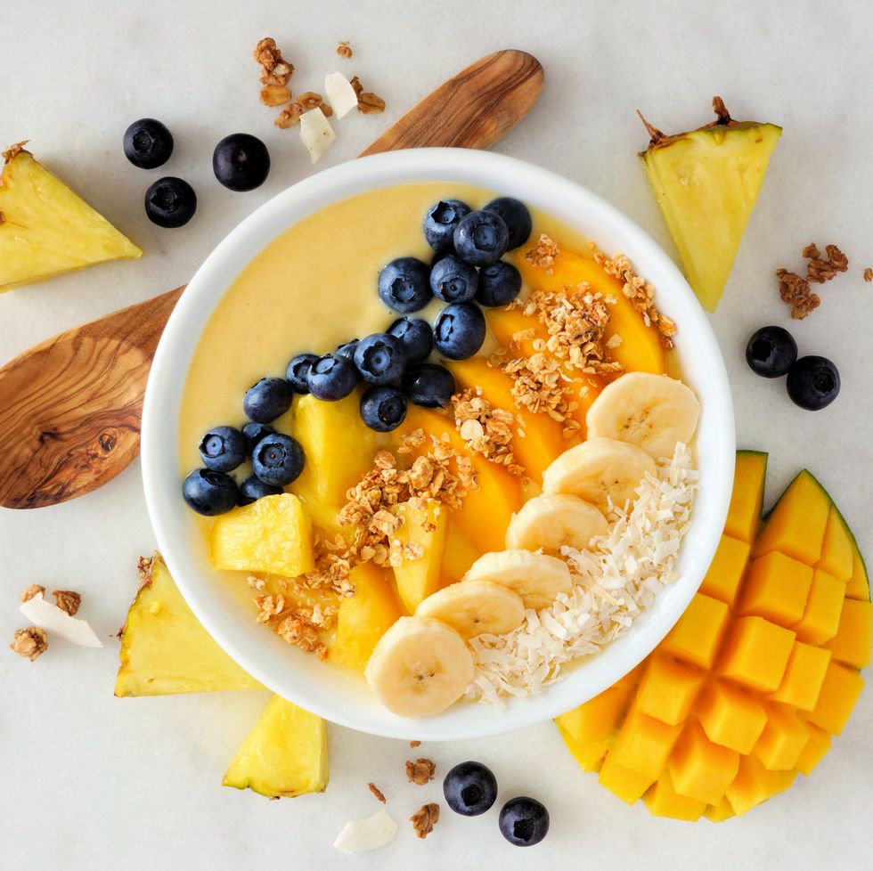 what to eat during periods for energy healthy pineapple, mango smoothie bowl with coconut, bananas, blueberries and granola above view scene on a bright background