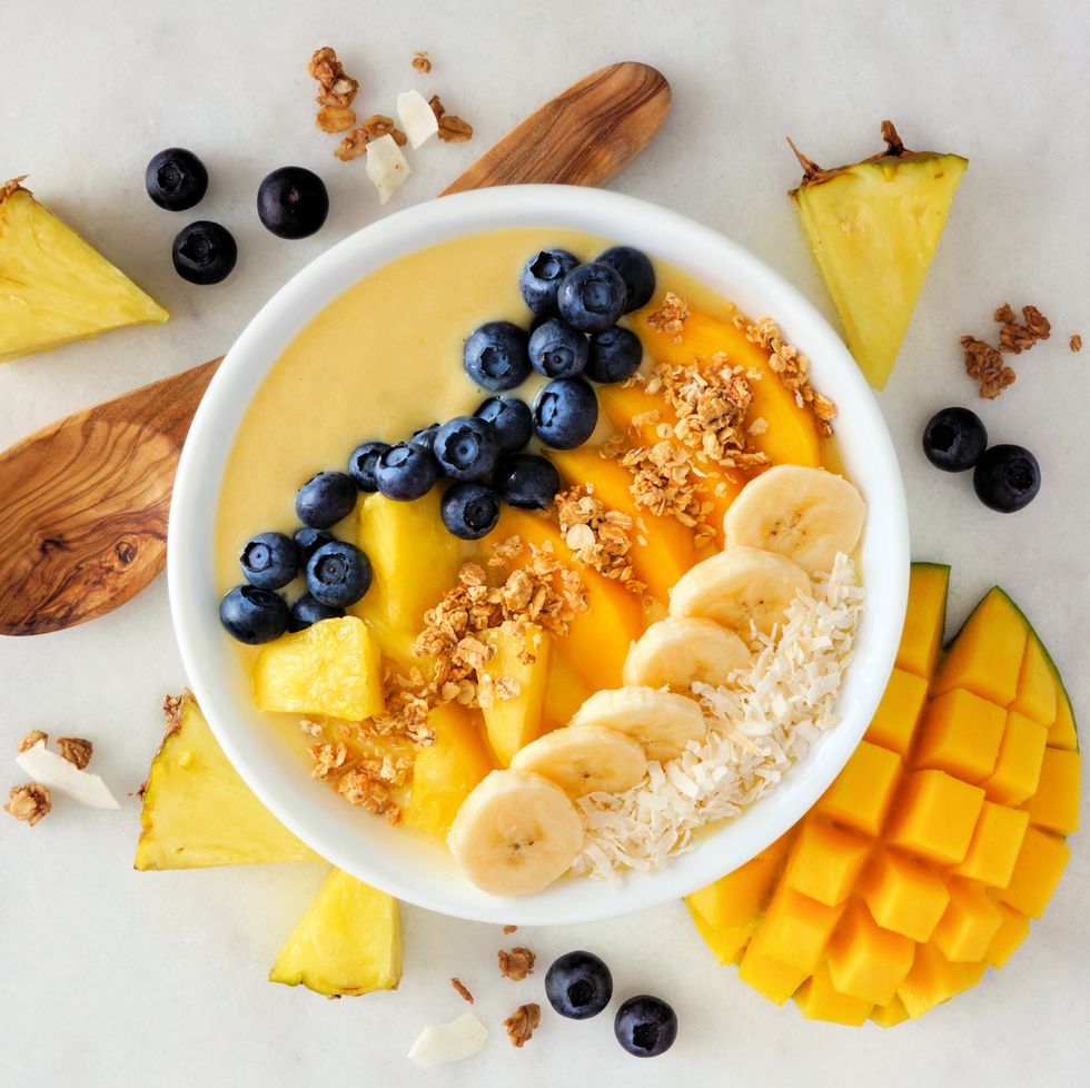 what to eat during periods for energy healthy pineapple, mango smoothie bowl with coconut, bananas, blueberries and granola above view scene on a bright background