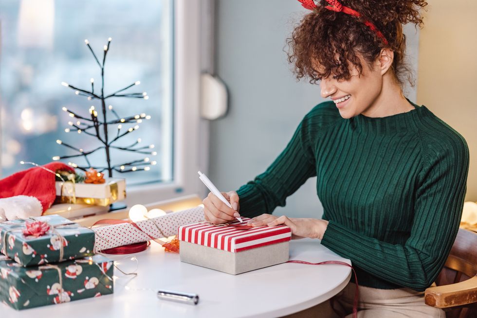 young woman preparing christmas gifts for family, she is writing christmas card