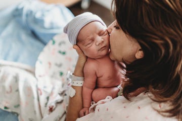 mother kissing newborn son baby on the cheek while in the hospital