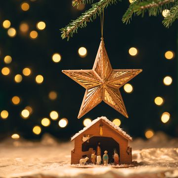 a manger sitting under a star ornament that is hanging from a christmas tree with lights blurred behind