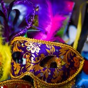 purple mardi gras face mask with orange pattern and yellow pink feathers in background