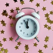 white alarm clock and star confetti on pink delicate background for holiday time