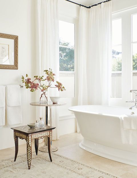 sheer embroidered draperies filter sunlight to a deep soaking tub atop neutral stone floors