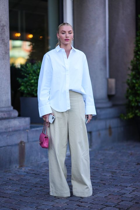 copenhagen, denmark, august 11, a guest wears gold earrings, an oversized white shirt, beige wide-leg jeans, gold rings, a pink shiny leather mini bag and eternal grain by chanel, pots outside during Copenhagen Fashion Week Spring Summer 2021 in August August 2022 Copenhagen Denmark Photo by edward berthelotgetty images