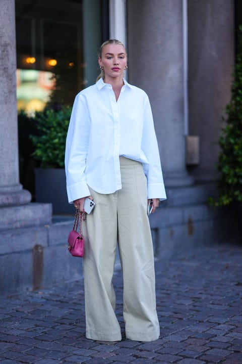 COPENHAGEN, DENMARK AUGUST 11 Exotic gold earrings, white oversized shirt, beige wide leg denim pants, gold rings, pink glitter grain leather mini timeless handbag from Chanel, sax jars outside at Copenhagen Fashion Week Spring Summer 2023, August 11 A.  2022 in Copenhagen, Denmark Photo by Edward Bertheloghetti Images