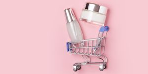 white cosmetic jars with cream lie in a shopping trolley on a pink background