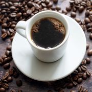 white cup with strong black coffee on a rustic wooden table with some beans, copy space, selected focus