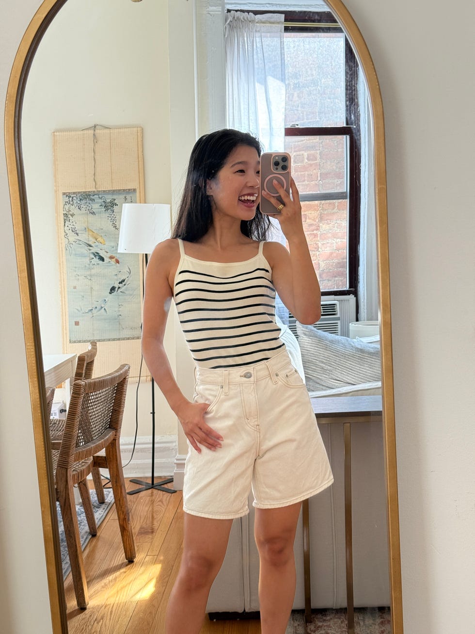 a person posing in front of a mirror wearing a striped tank top and white shorts