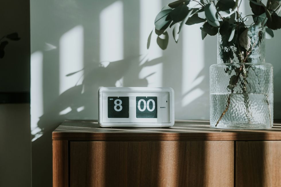 a white digital flip clock shows eight o'clock on a brown wooden cabinet next to fresh eucalyptus plant in the living room, with sunbeam shining through the window on a fresh beautiful morning. a brand new day, fresh start, fresh energy, new opportunities