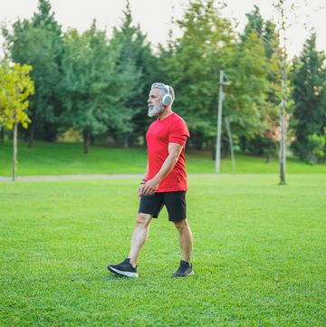 white haired man in red tshirt listening to music and walking in the park
