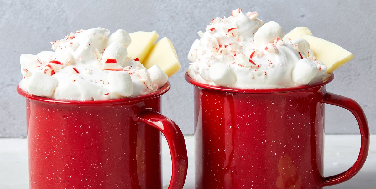 white hot chocolate in red mugs topped with whipped cream, crushed peppermint candies, white chocolate pieces, and mini marshmallows