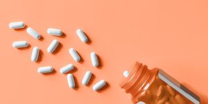 white pills spilling out of prescription bottle onto orange surface