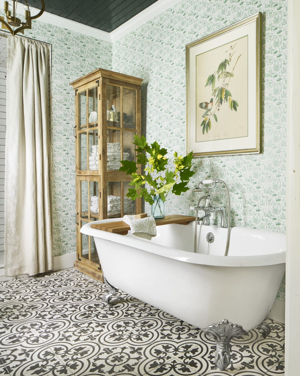 white clawfoot bathtub in a bathroom with green and white toile wallpaper and black and white tile