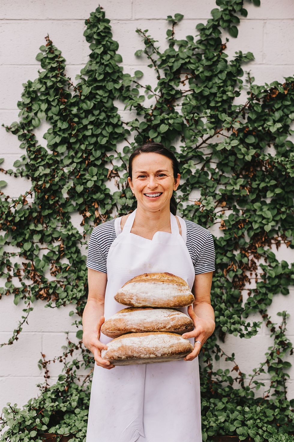 woman wearing striped shirt and apron holding loaves of bread