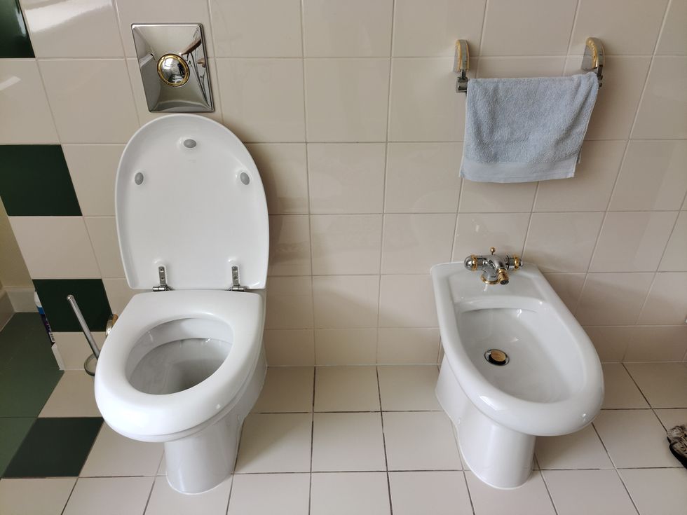 white toilet and bidet in the toilet above them is a towel and a water drain button ceramic tiles on the walls an example of decor and interior