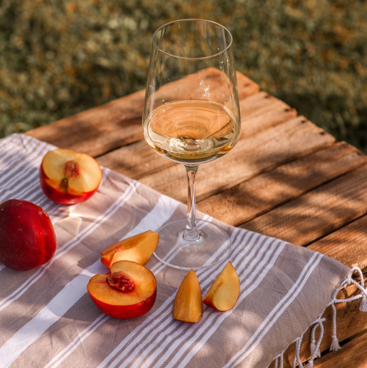 white wine glass in summer garden with peaches on wooden crate picnic