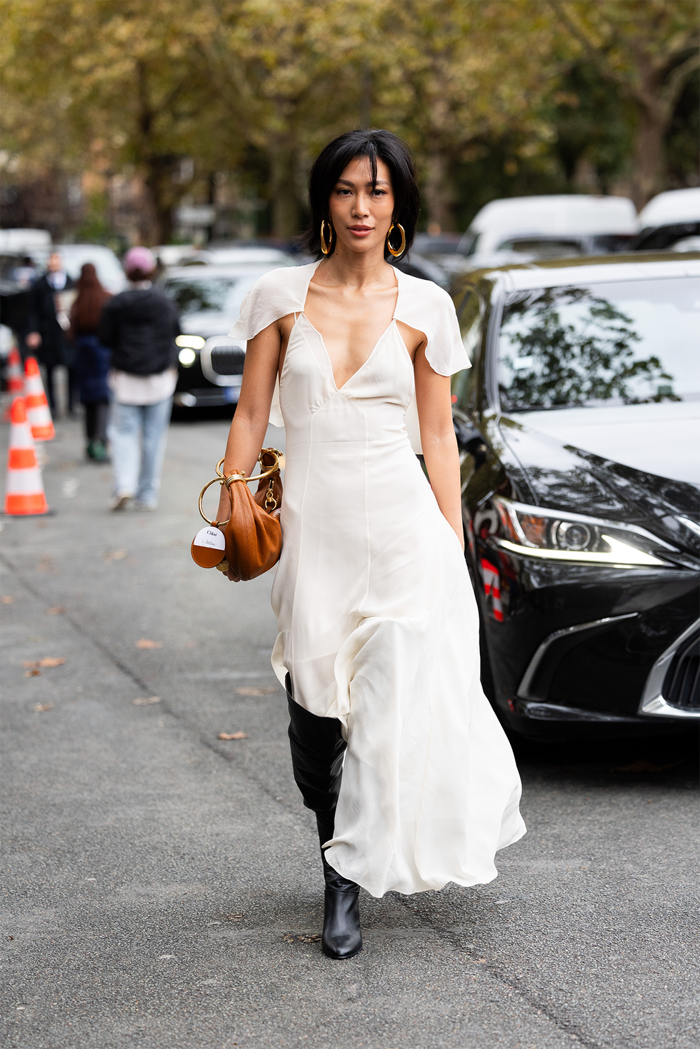 paris, france september 26: molly chiang wears black leather knee high heeled boots, gold hoop earrings, a brown and gold leather bag and a white sleeveless with a cape long dress outside chloé show during womenswear spring/summer 2025 as part of paris fashion week on september 26, 2024 in paris, france. (photo by valentina frugiuele/getty images)