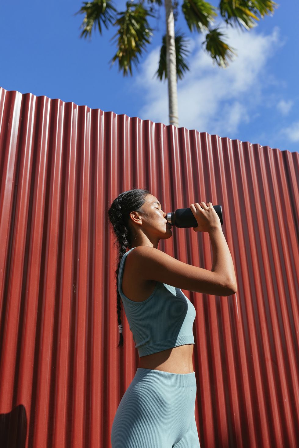 woman standing in front of the red wall and drinking water