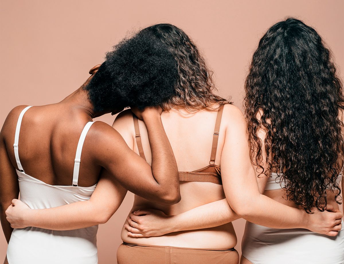 three femmes with their backs facing the camera embracing each other with arms wrapped around each other