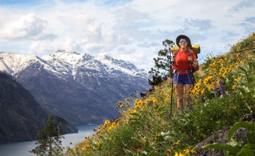 aj williams backpacking in a field of flowers with snowy mountain caps in the background