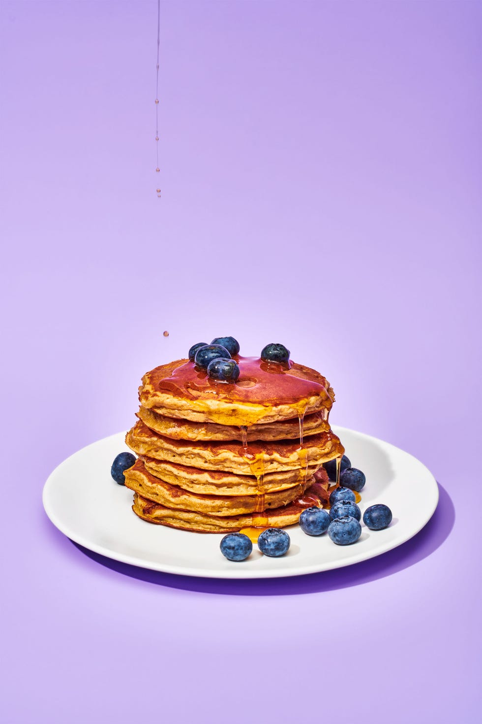 stacked pancakes on a plate with blueberries and syrup pouring on them, on a background