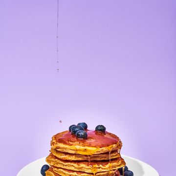 stacked pancakes on a plate with blueberries and syrup pouring on them, on a background