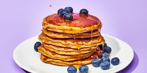 stacked pancakes on a plate with blueberries and syrup pouring on them, on a background