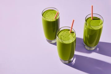 three glasses of green smoothie with pink straws on a purple surface