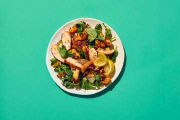 a plate of grilled chicken with vegetables and lemon slices on a bright background