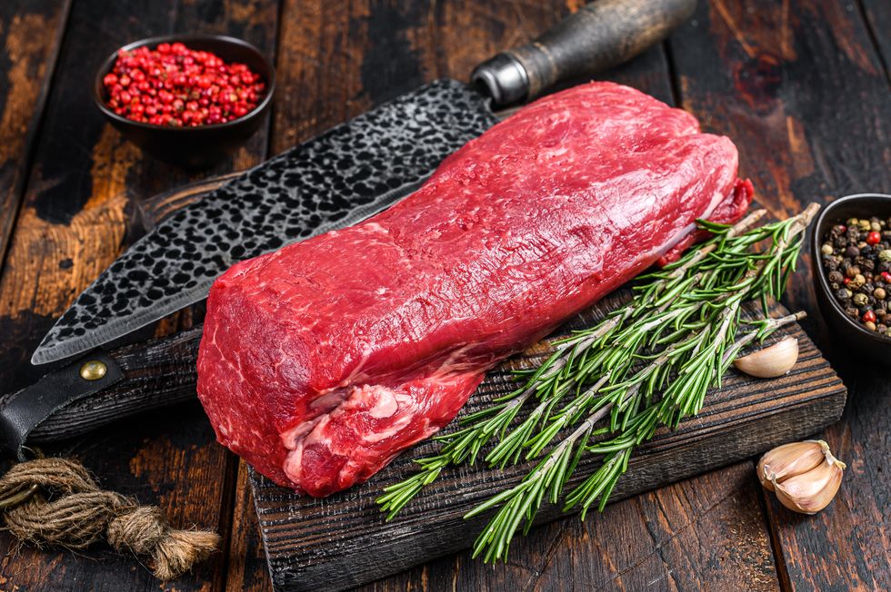 whole raw tenderloin beef meat for steaks fillet mignon on a wooden cutting board with butcher knife dark wooden background top view